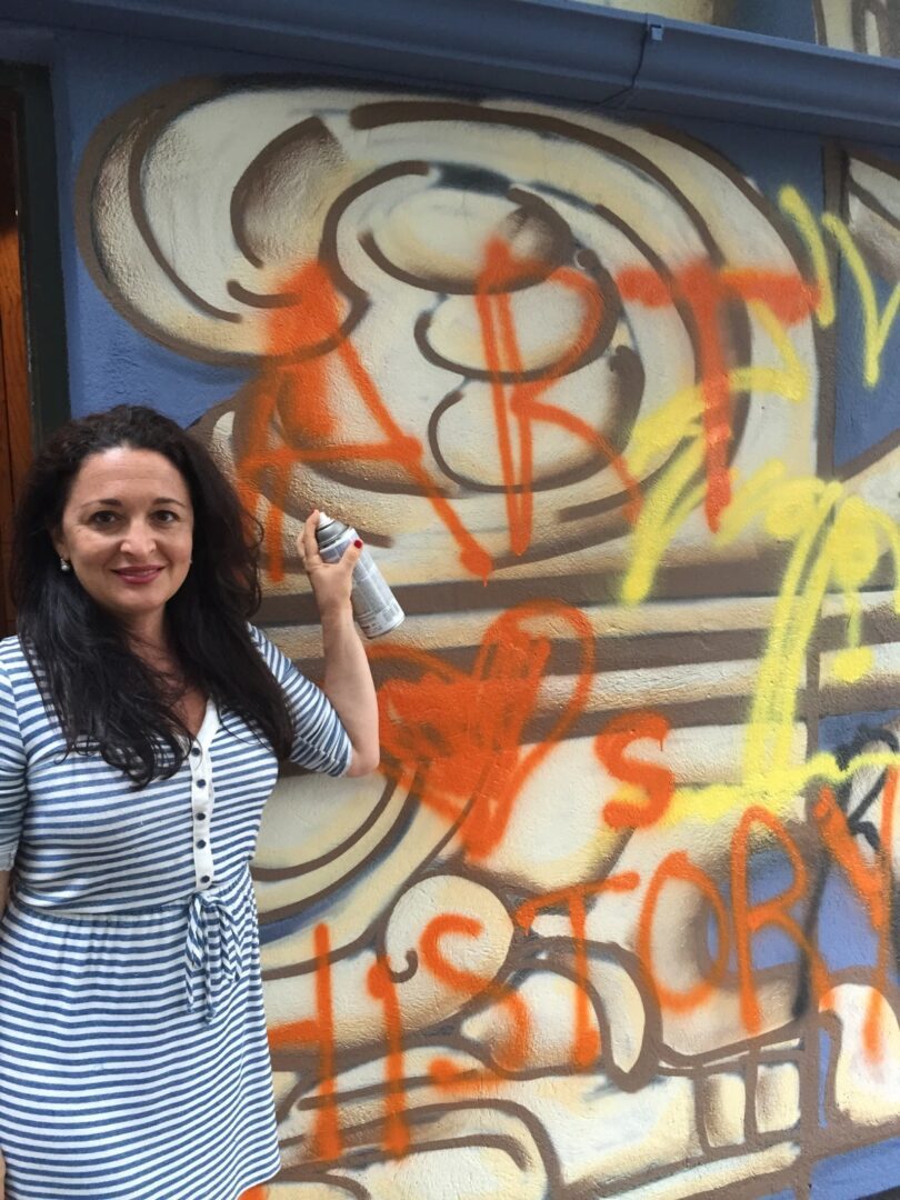 A woman is standing in front of a wall with graffiti.